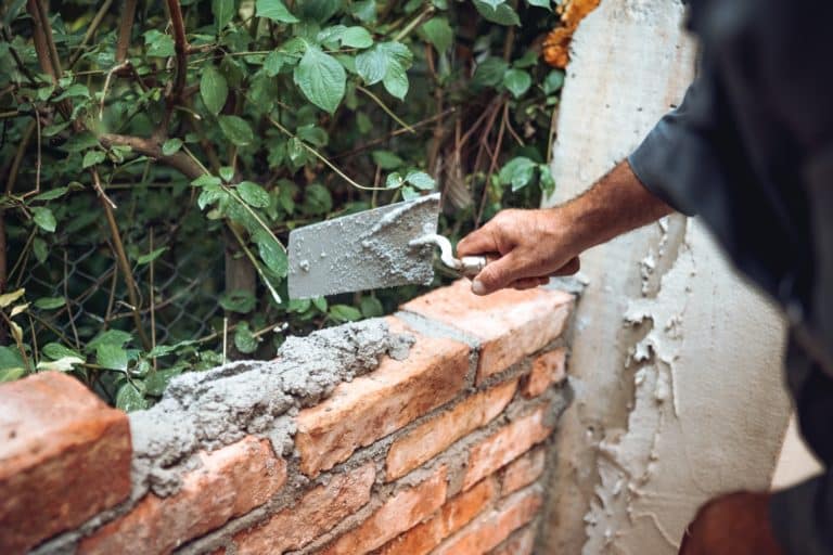 bricklayer placing and adjusting bricks with mortar.